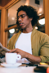 Bewildered man reading newspaper while drinking coffee in cafe