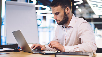 Caucasian male employee reading web information on browsed site survey during productive working process at office table, skilled businessman using 4g internet for making online banking and booking