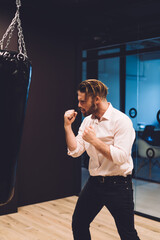 Caucasian worker in smart casual clothing punching boxing bag disappointed with miss fortune...