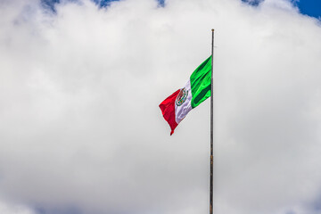 Mexican flag waving with a blue sky and a large cloud in the background