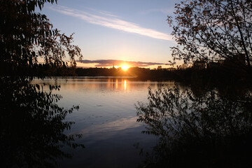 Obraz premium Natural landscape with beautiful sunset on the river and branches silhouettes on the waterside against calm water