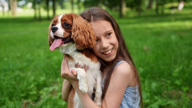 Happy girl holding and hugging cute cavalier king charles spaniel puppy while walking outside. Young owner and her pet. Concept of love, caring for dog, pet care. 
