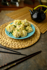 A plate of freshly steamed dumplings garnished with herbs, served with a black teapot and chopsticks on a rustic table setting. Mongolian Food: Buuz (Steamed Mongolian Dumplings)