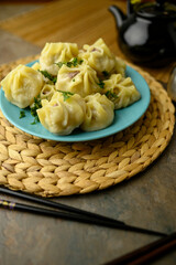 A plate of freshly steamed dumplings garnished with herbs, served with a black teapot and chopsticks on a rustic table setting. Mongolian Food: Buuz (Steamed Mongolian Dumplings)