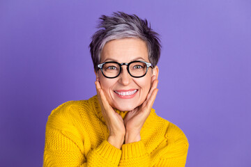 Smiling mature woman in yellow sweater with glasses against purple background