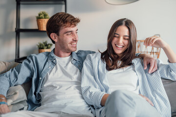 Young happy couple having fun talking laughing relaxing at home on couch, boyfriend embracing...