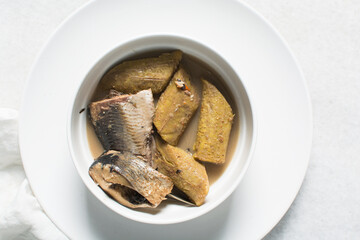 Overhead view of Nigerian pepper soup with fish and plantain in a white soup plate, top view of fish pepper soup in a white plate