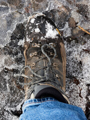 A closeup of a rugged hiking boot stepping cautiously on icy terrain.