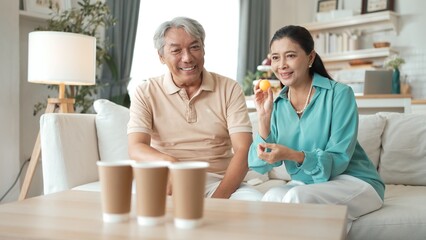 Happy elderly couple enjoying a ball toss game together at home, practicing coordination and cognitive skills for healthy aging. Grandfather and grandmother throwing ping pong in the bowl. Myrmidon.