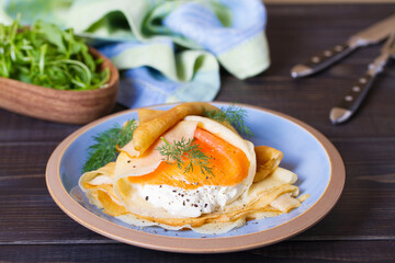Wrapped thin pancake with filling - smoked salmon and cream cheese and pancake with scrambled egg and salmon. Crepes on blue plates