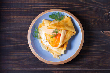 Wrapped thin pancake with filling - smoked salmon and cream cheese and pancake with scrambled egg and salmon. Crepes on blue plates. View from above, top view