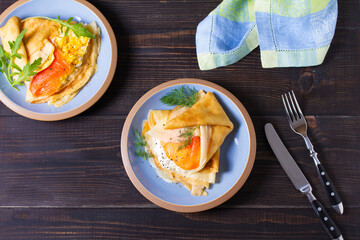 Wrapped thin pancake with filling - smoked salmon and cream cheese and pancake with scrambled egg and salmon. Crepes on blue plates. View from above, top view