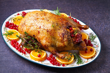 Roasted duck served with oranges and red currants on white plate on dark background. View from above, top view with copy space