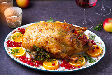 Roasted duck served with oranges and red currants on white plate on dark background. View from above, top view with copy space