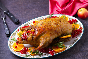 Roasted duck served with oranges and red currants on white plate on dark background. View from above, top view with copy space
