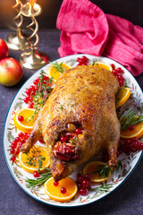 Roasted duck served with oranges and red currants on white plate on dark background. View from above, top view with copy space