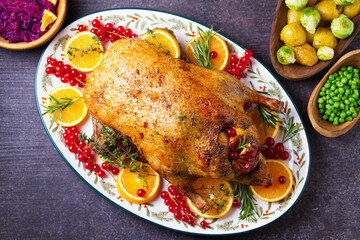 Roasted duck served with oranges and red currants on white plate on dark background. View from above, top view