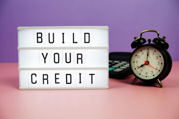 Build Your Credit letterboard text on LED Lightbox with alarm clock and calculator on pink and purple background