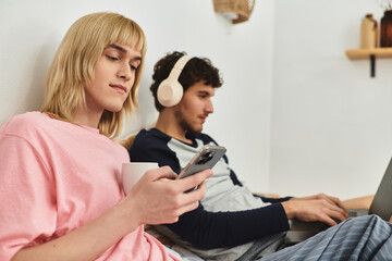 Two loving men spend a comfortable evening together, engaging with their devices and each other.