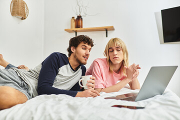 Two men share a relaxed evening together, smiling and interacting while using a laptop comfortably.