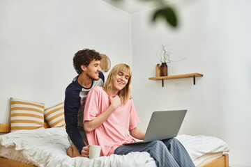 Two men share a joyful moment together at home while working on a laptop, radiating warmth and love.