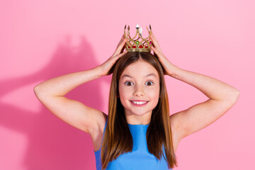 Adorable young girl with a crown smiling joyfully against a pink background © deagreez