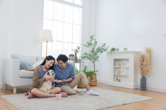 Asian couple spends quality time with their pug dog in their living room