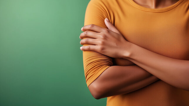Woman in orange shirt holding crossed arms against green background. Body language and communication content