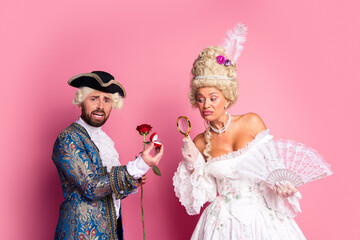 Elegant couple in royal inspired costumes posing against a bright pink background