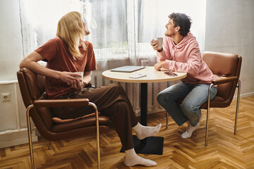 Fototapeta premium Two loving men sit together in a sunny room, sharing smiles and coffee at a small table.