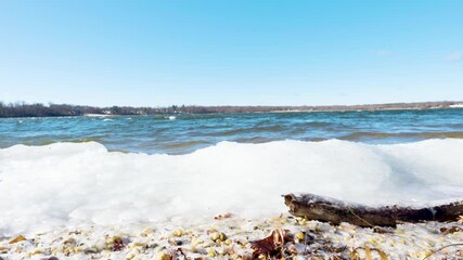 A peaceful winter scene at Lake Ronkonkoma, Long Island. Clear blue skies reflect over shimmering icy waters, creating a tranquil moment of natural beauty. Captures the serene charm of the season.