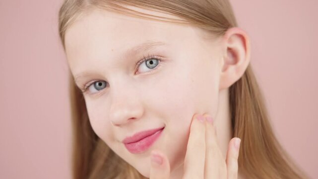 Portrait of a beautiful cute young girl taking care of her face skin. Blonde Caucasian girl with blue eyes isolated on pink background. Advertising concept of skin care for teenagers. Acne treatment.