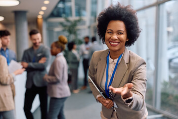 Happy black presenter welcoming business seminar attendees at convention center and looking at camera.