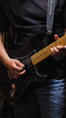 Musician in black clothes and blue jeans playing a black electric guitar with maple deck, green...