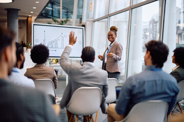 Happy black businesswoman aiming at one of colleagues who wants to ask a question during conference...