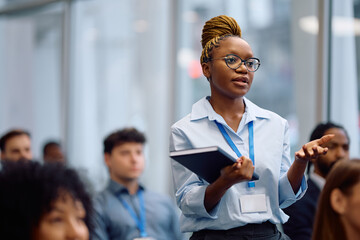 Black female business seminar attendee talking from audience at convention center.
