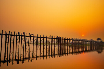 Silhouette of U Bein bridge at sunset in Myanmar.  and reflecting bridge the water