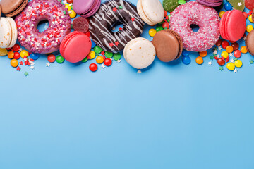 Obraz premium An assortment of colorful sweets, including donuts, macarons, and candies, arranged on a vibrant blue background