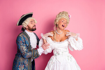 Elegant couple in royal costume enjoying a glamorous masquerade event with a pink backdrop