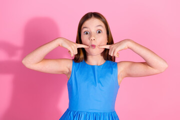 Charming young girl with a playful expression in a blue dress against a pink background