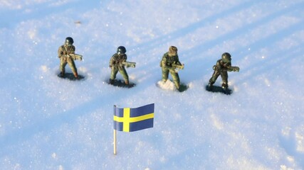 Small Swedish flag in the snow. Green toy soldiers in the background. Concept photo. Winter war.
