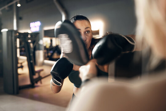 Fit young woman wearing a tank top and boxing gloves practicing punches with a female partner during a self defence workout session together in a gym