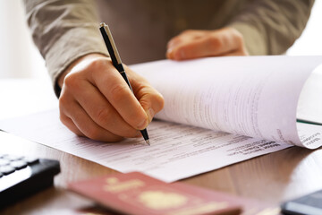 Close-Up of Hand Filling Out Forms with Pen and Passport on Desk