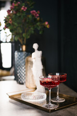 Gold tray with two glasses of red wine and a statue of a woman. Scene is elegant and sophisticated