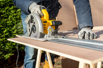 Male using electric circular saw to cut DIY sheet material outside