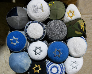 A variety of colorful, patterned, knit Jewish yarmulkes or skull caps for sale in a religious neighborhood of Jerusalem.
