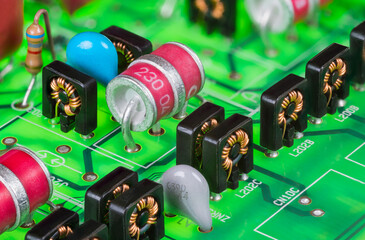 Red electrode gas discharge surge arresters and toroid inductors in black case. Closeup of electronic components on green printed circuit board in digital telephone switch analog part line protection.