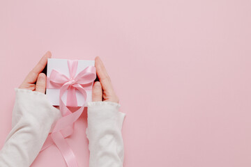 Cute gift box in woman hands with copy space on pink background, valentine gift, mother and woman day
