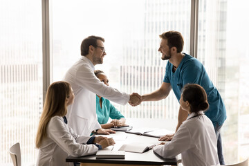 Formal meeting in clinic board-room among medical employees, finishing with handshake gesture,...