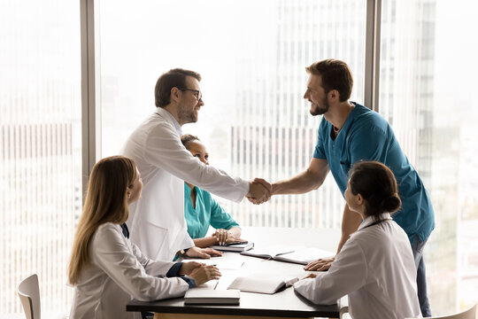 Formal meeting in clinic board-room among medical employees, finishing with handshake gesture, concluding professional collaboration. Teamwork in healthcare, professional opinion exchange, greeting